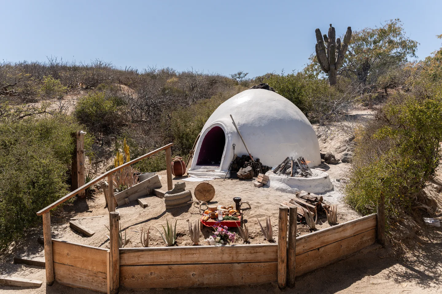 White temazcal dome and altar among desert plants — NEST Baja