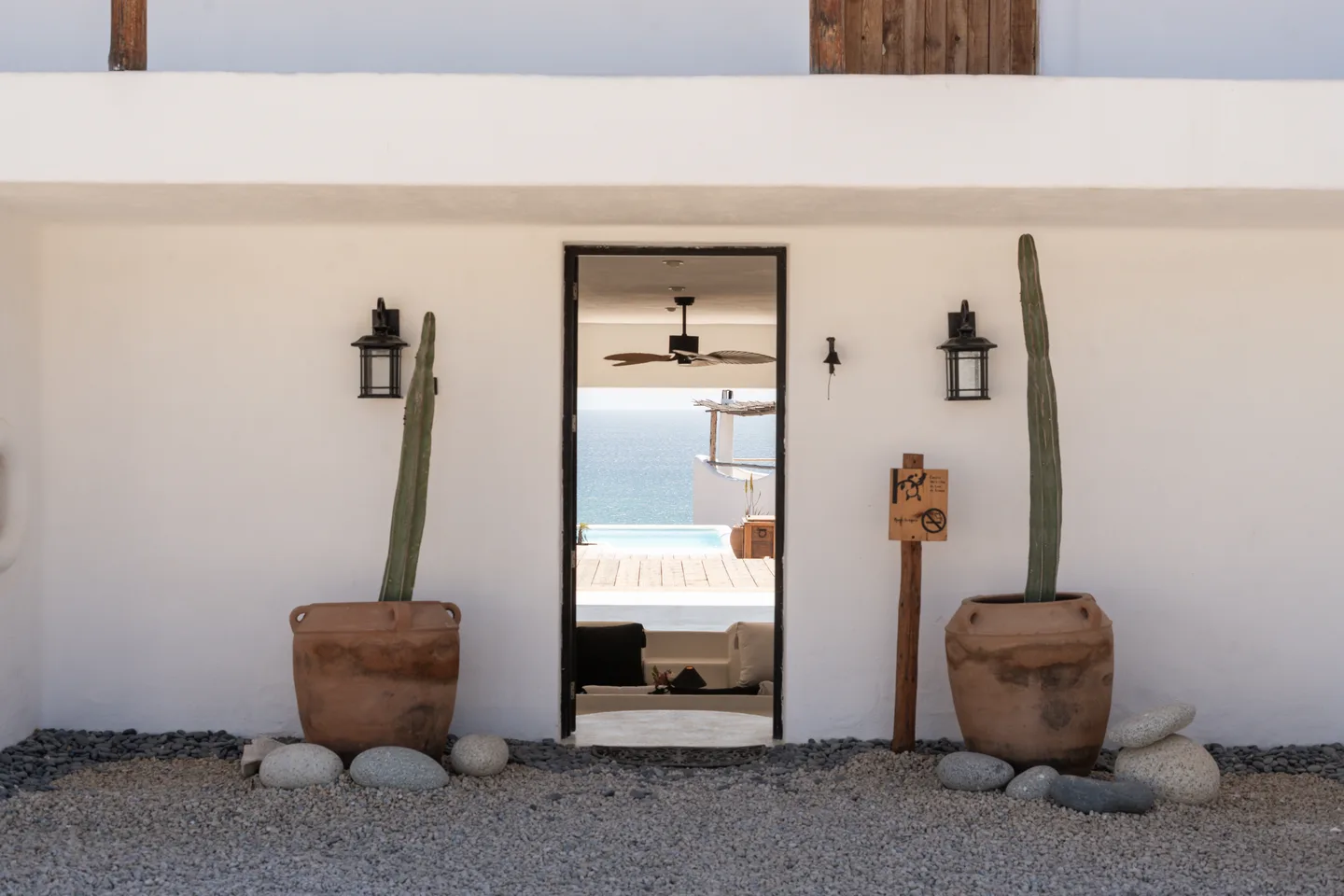 Entrada del lobby enmarcada por cactus en maceta y faroles — NEST Baja