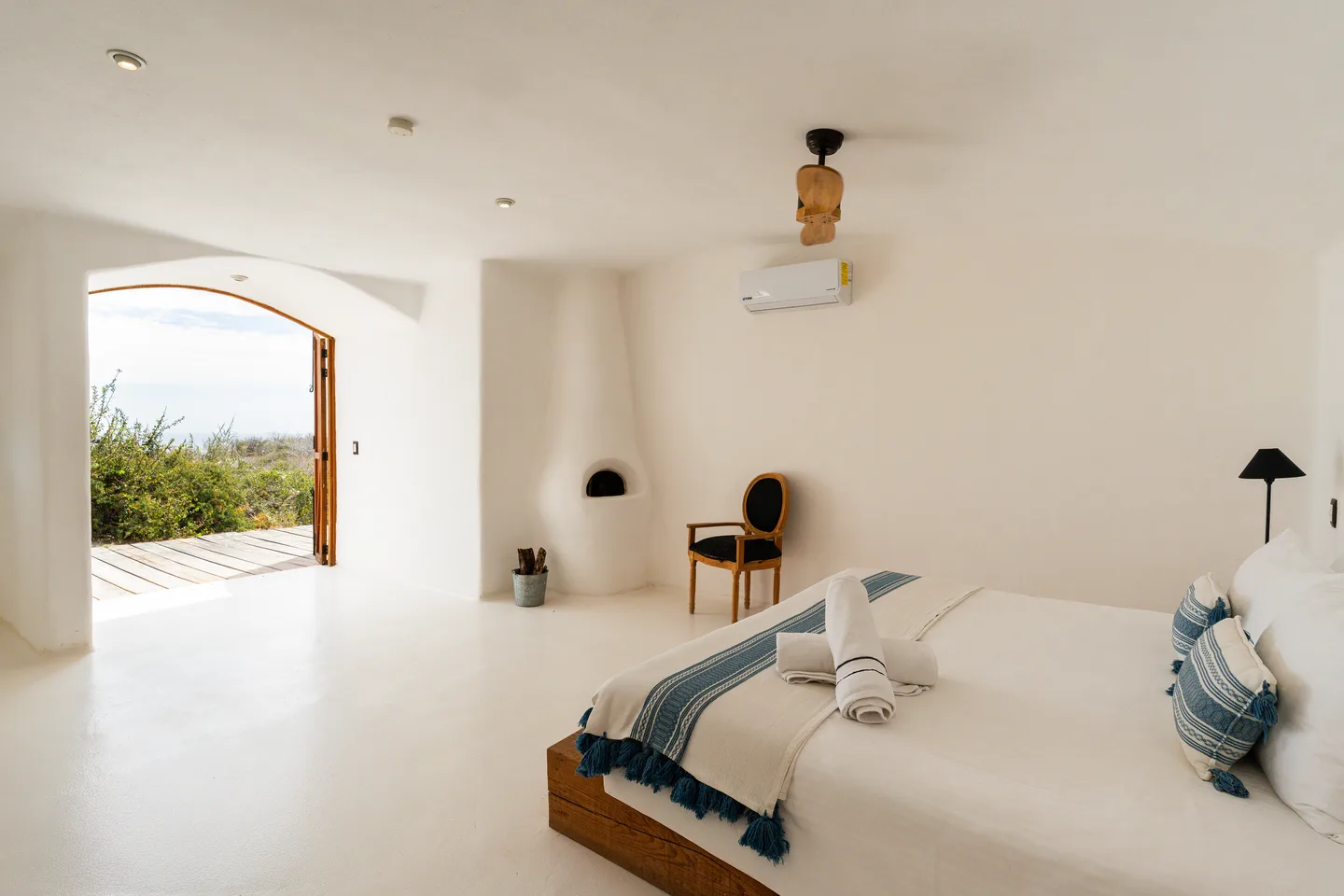 Recámara con chimenea azteca y puertas arqueadas de madera abiertas a la terraza — NEST Baja