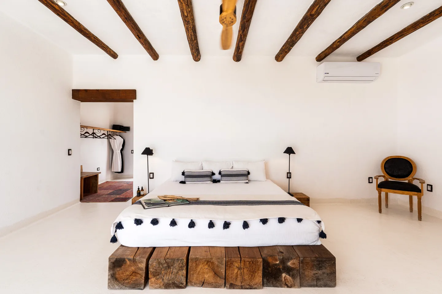 Cama king con colcha de borlas negras y armario abierto — NEST Baja