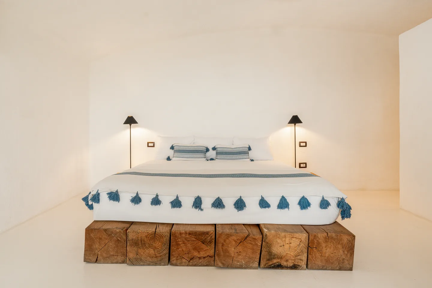 Cama king con colcha de borlas azules entre lámparas de noche — NEST Baja