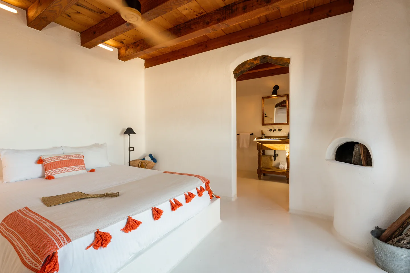 Recámara con cama king, cobertor con borlas color coral, techo de vigas y chimenea Azteca — NEST Baja